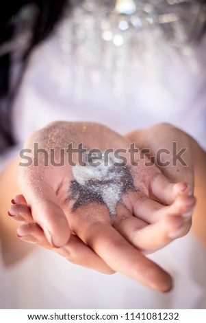 White and silver glitter in palm of hands closeup woman holding glitter in open hands wearing white dress