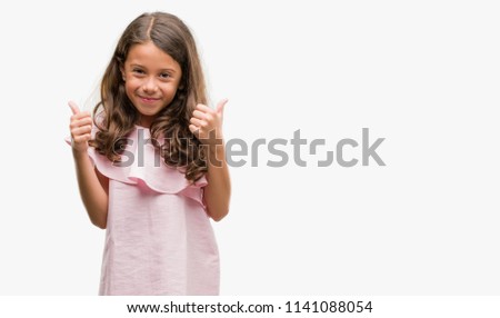 Brunette hispanic girl wearing pink dress success sign doing positive gesture with hand, thumbs up smiling and happy. Looking at the camera with cheerful expression, winner gesture.