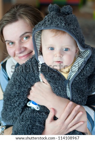 Sweet baby boy in warm winter clothes with mother on background