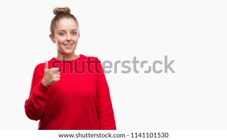 Young blonde woman wearing bun and red sweater doing happy thumbs up gesture with hand. Approving expression looking at the camera with showing success.