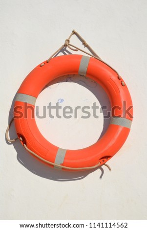 The red/orange lifebuoy hanging on white wall on a sunny day