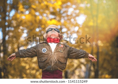 Child playing in a pilot aviator with toy airplane outdoors in autumn park. Dreams of flight and travel. Sunset.