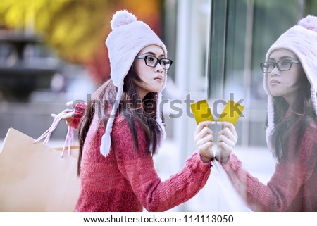Portrait of young girl carrying shopping bag and holding a card. shot outdoor with reflection on the glass