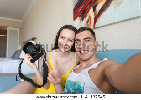 Selfie of a young couple in the room in the hands of a DSLR and a symbol of peace.