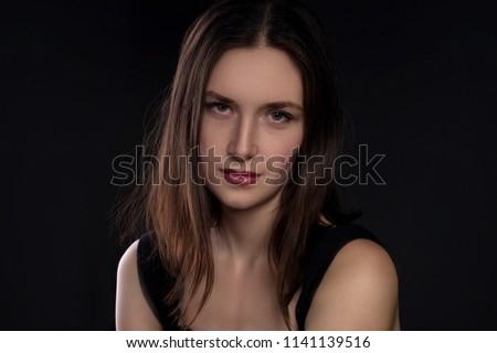 Close up portrait of the young woman  brunette wearing black dress in studio on dark background