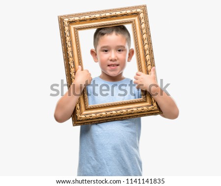 Dark haired little child holding frame with a happy face standing and smiling with a confident smile showing teeth