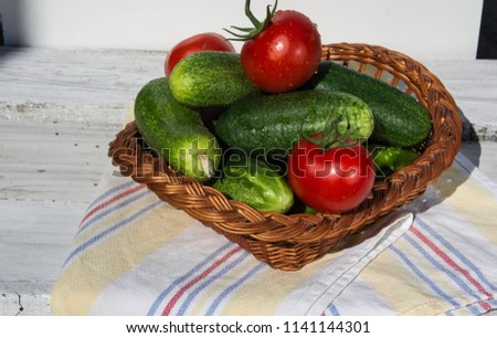 Ferney Voltaire, Rhone Alps France - July 2018:  Fresh green cucumbers and tomatous in a wicker basket on a table of boards ready to eat.
