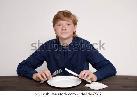 Portrait of a cute eating teenager on a white background at the table. He sits right in front of the camera smiling and looks happy