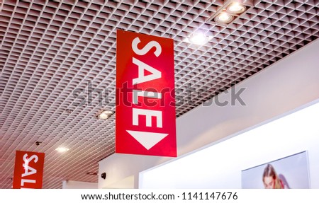 two rows of vertical sale posters with white letters hang from grid ceiling in big shop in sale season. sale poster board at fashion clothes shopfront