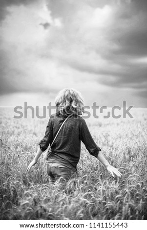 woman in a wheat field. year-old black and white landscape. the figure of the girl in the ears of wheat. Royalty-Free Stock Photo #1141155443