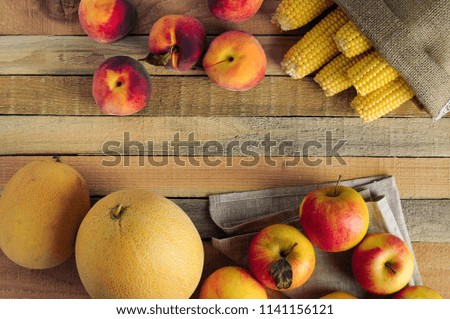 Fresh corn, apples, peaches and melons on rustic wooden background. Warm still life with free space for Your text.