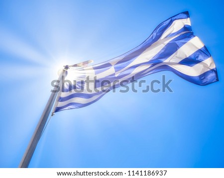 Official flag of Greece waving on a blue sky and sunlight rays.