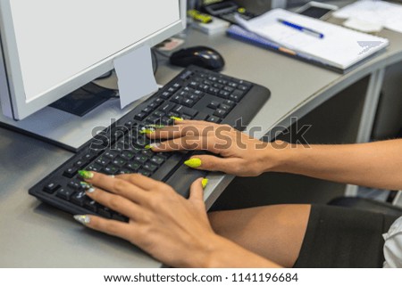 girl with beautiful manicure runs on a computer and writes on a keyboard. a typist or receptionist running on a computer. a blank screen on a monitor and a stuck note for reminders.