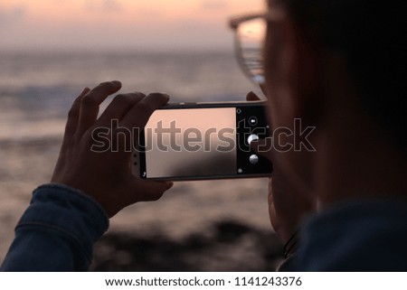 A young woman photographs with her smart phone a sunset at sea