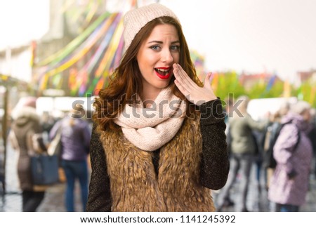 Girl with winter clothes making surprise gesture on unfocused background