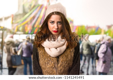 Sad girl with winter clothes on unfocused background
