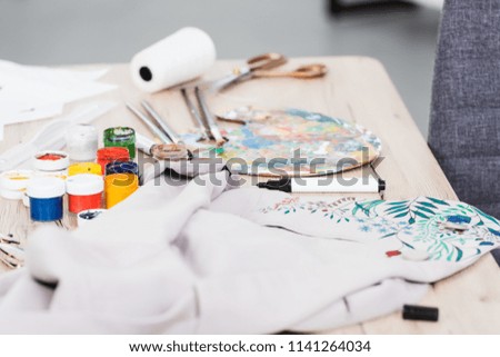 selective focus of colorful paints and painting jacket at table in clothing design studio 