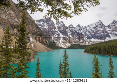 Canadian landscape, with turquoise water lake, forest of pine trees and Rocky Mountains on background, and rock wall and trail sign on foreground, in Lake Moraine, Banff National Park, Alberta, Canada