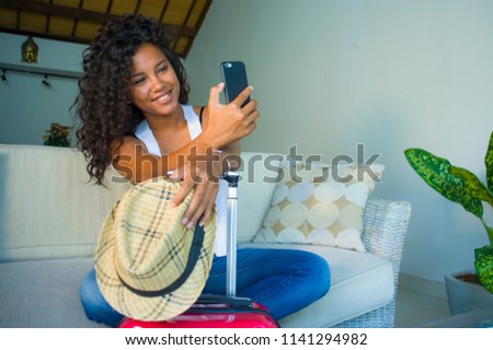 young attractive and happy black hispanic woman at home with suitcase sitting on sofa couch leaving for holidays trip feeling excited smiling cheerful in tourism and vacations travel concept