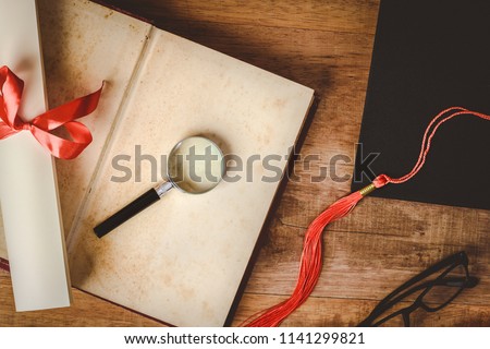 magnifying glass and diploma tied with red ribbon on open old book blank, top view