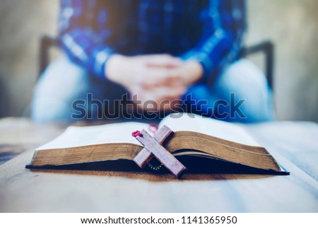 wooden cross over open bible with blurred of man praying, Christian background.
