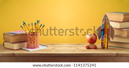 Back to school background with rocket made from pencils, apple and old books over yellow wall