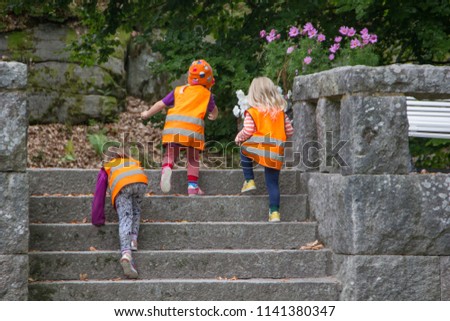 Unidentifiable Swedish kindergarten children playing and running up the stairs of a park. For safety reason, kids have to wear a reflecting safety west in orange with reflector batches placed on them Royalty-Free Stock Photo #1141380347