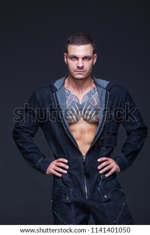 The man with a muscular torso with tattoos on the dark background