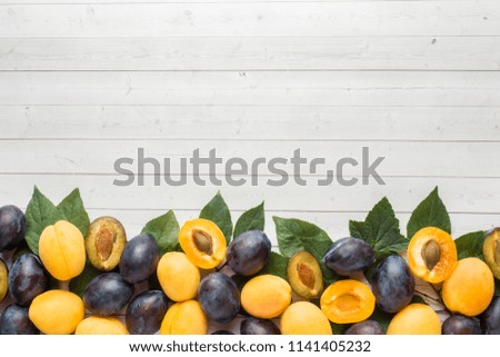 Fresh plum and apricot berries with leaves on a light table