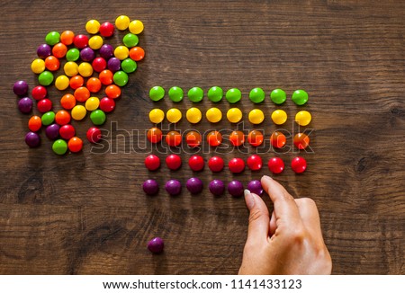 woman's hand collects even row of colorful candies on a wooden background Royalty-Free Stock Photo #1141433123