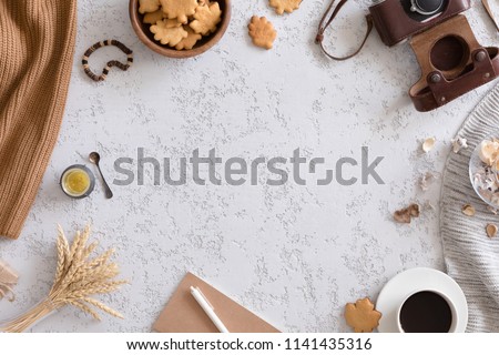 Hello Autumn flat lay background. Top view of workspace or office desk with vintage photo camera, sweater, cup of coffee, honey cookies, flowers and gold ears of wheat on textured white background