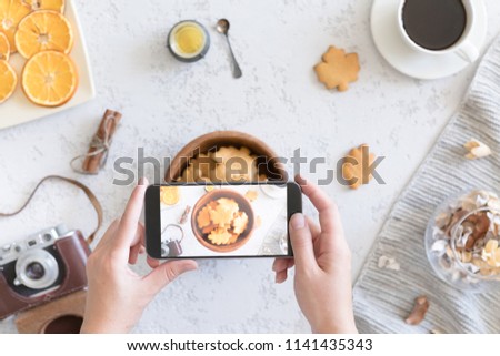 Flat lay of cozy autumn breakfast with homemade honey cookies and cup of tea, top view of woman hand takes pictures of food on the phone