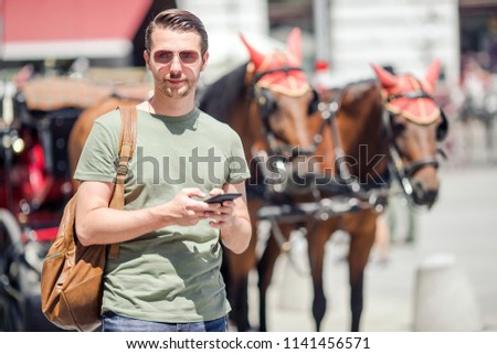 Young man with smartphone in the city backgroundof traditional horses in carriage outdoors in Vienna