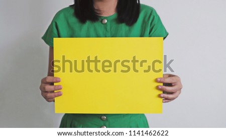 Asian woman in green vintage dress holding a blank yellow paper for messages or copy space e.g. SHOP NOW, ON SALE, GIRL POWER, SUCCESS, BE CAREFUL!, BE QUIET!, International women’s day concept.