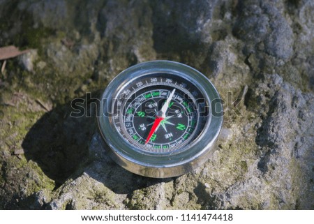 A metal compass placed on a rock in the sunlight, casting a shadow.