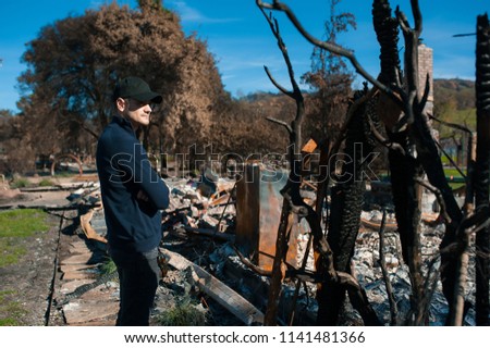 Man owner checking burned and ruined house and yard after fire, consequences of fire disaster accident. Ruins after fire disaster, loss and despair concept.