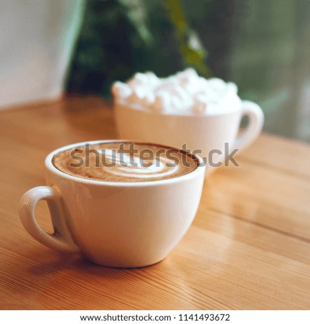 Two cups of cappuccino with latte art and marshmallow on wooden background. Beautiful foam, greenery ceramic cups, stylish toning, place for text.