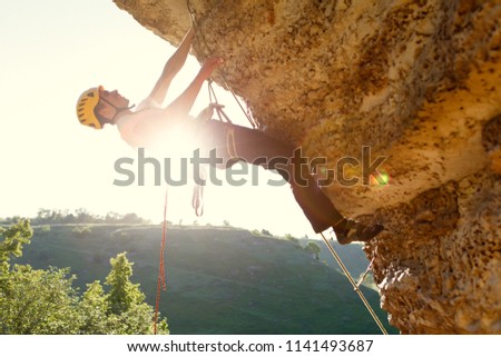 Picture of man climber in helmet clambering up cliff.