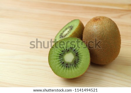 Closed up cross-sections of fresh ripe kiwi fruit with a whole fruit isolated on wooden table