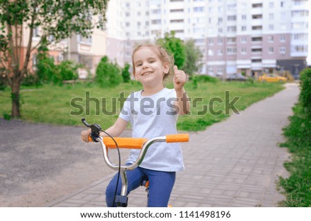little girl riding her bike. concept of health. the child shows good, the girl in the gray shirt is a thumbs up.