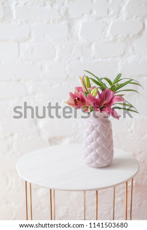 Purple lily flowers bouquet in pastel pink vase on white empty coffee table