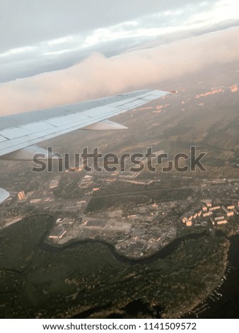 A view from above of the city with buildings, houses from the porthole, aircraft windows on the wing with engines, turbines and white fluffy, rain clouds.