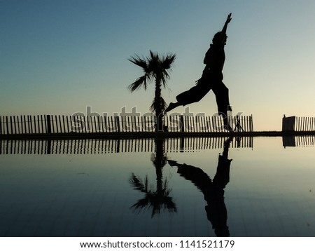 single woman with wide trousers as silhouette jumping at a pool during sunset in morocco