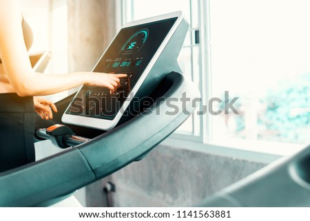 Young attractive woman pressing on screen control menu machine for training workout in gym .Healthy sporty girl running on treadmill at panoramic window. Healthy lifestyle workout burning calories.