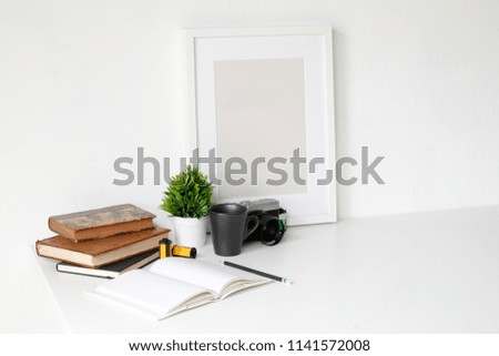 Work table with photography camera, book, notepad and pencil on white table and empty photo frame.
