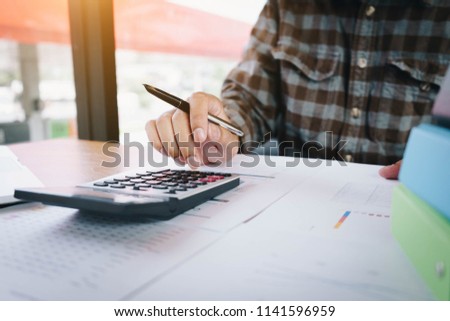 Business man holding pen and using smartphone for calculating financial marketing with calulator at workplace. Business finances and accounting concept. Royalty-Free Stock Photo #1141596959