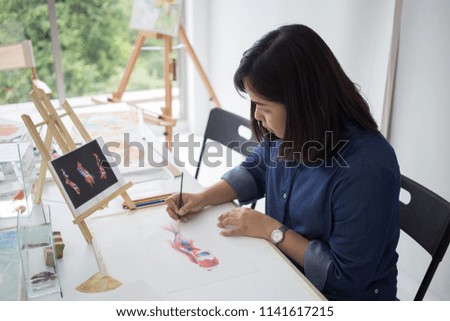 Woman artist painting fish picture in studio.