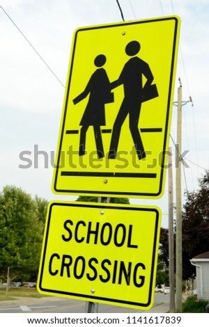 Closeup image of a school crossing sign posted outside the building as a street notification to drivers.