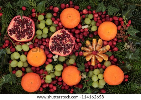 Christmas background of mandarin, pomegranate, green grape bunches and cranberry fruit, holly, mistletoe, ivy, spruce fir and cedar leaf sprigs with pine cones over white background.