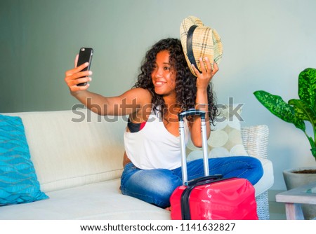 young attractive and happy black hispanic woman at home with suitcase sitting on sofa couch leaving for holidays trip feeling excited smiling cheerful in tourism and vacations travel concept